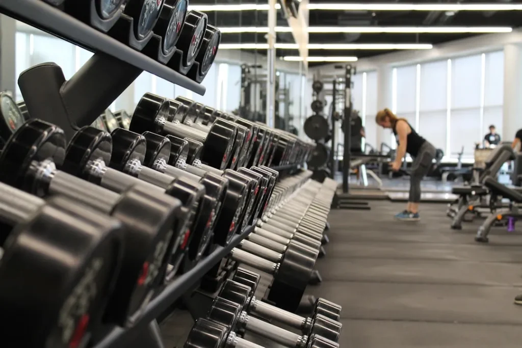 Rows of dumbbells in a modern gym with a person exercising in the background