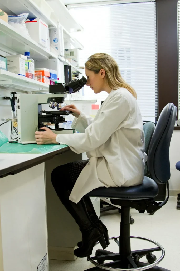 A female researcher in a white lab coat meticulously analyzes a compound under a professional microscope