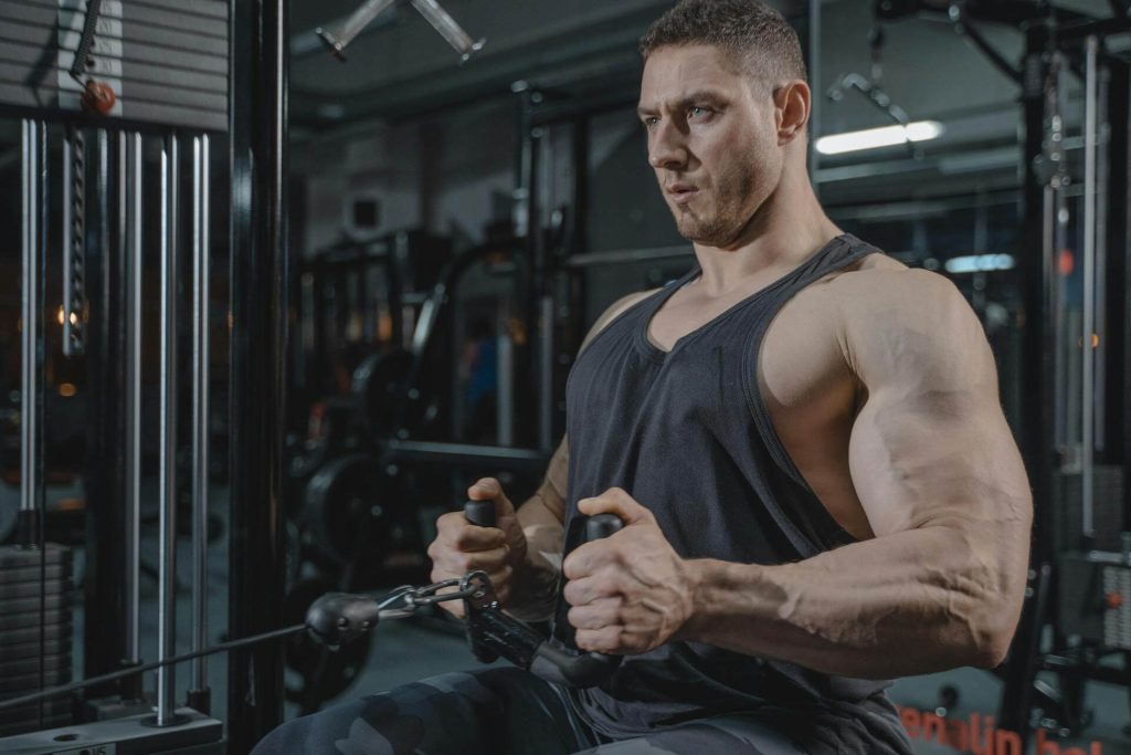 A muscular man in a black tank top performing a seated cable row exercise at the gym